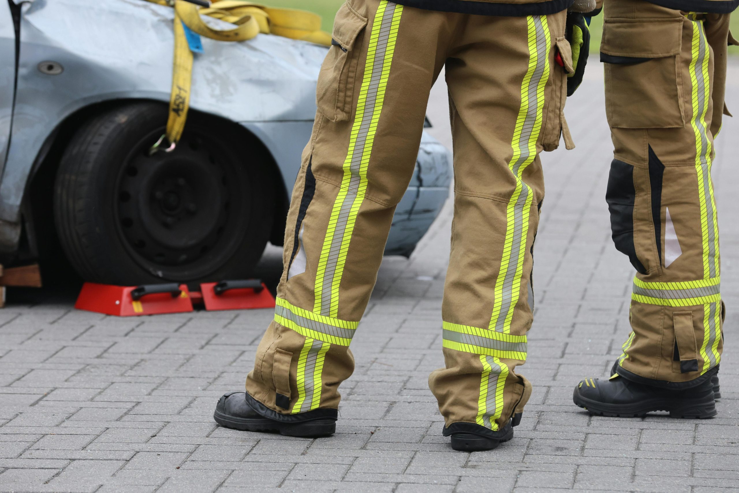 Home Firefighters inspecting a car accident wearing protective gear. Focus on pants and footwear.